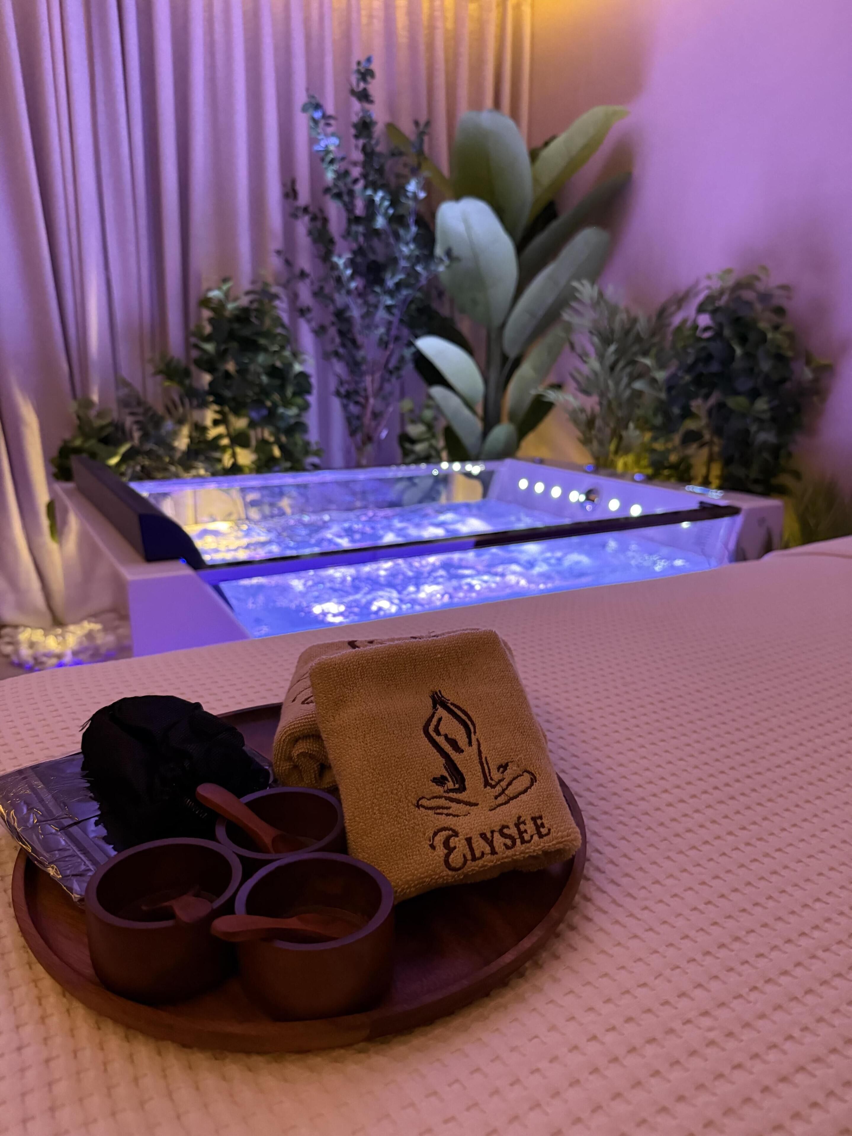 A spa setting with a massage table, a tray with a towel and cups, and a water feature in the background.