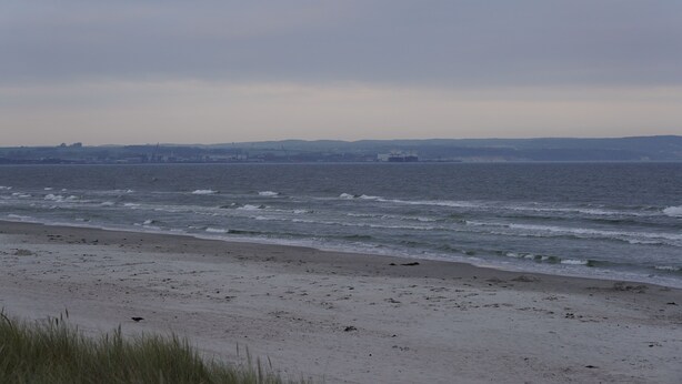 A beach with a view of the ocean and distant hills.