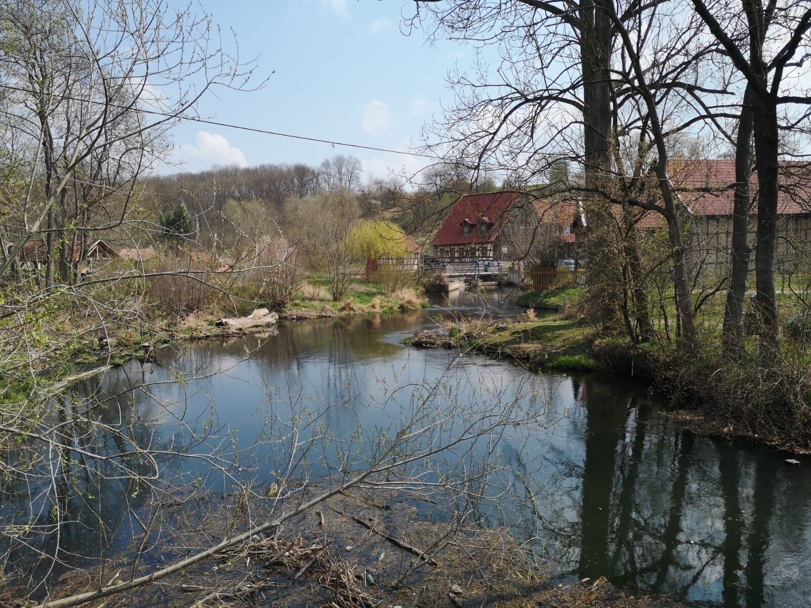 Un río tranquilo con un puente y una casa con tejado rojo al fondo.