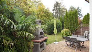 A patio with a stone barbecue, a table and chairs, and a green umbrella.