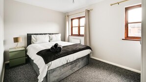 Un dormitorio con cama, mesita de noche, lámpara y ventana.