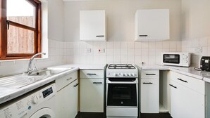 Una cocina compacta con armarios blancos, estufa a gas, microondas y lavadora.