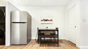 A compact kitchen with a stainless steel refrigerator, a dining table with chairs, and a wooden floor. - 3 BedHome in Upper Lawrenceville (Pittsburgh)
