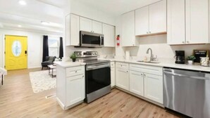 A modern kitchen with white cabinets, stainless steel appliances, and a wooden floor. - 3 BedHome in Upper Lawrenceville (Pittsburgh)
