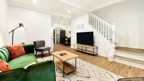 A modern living room with a green sofa, a coffee table, a TV on a stand, and a staircase. - 3 BedHome in Upper Lawrenceville (Pittsburgh)