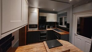 A compact kitchen with white cabinets, a wooden countertop, and a built-in oven. - Cozy Blackpool Retreat With 3 Bedrooms (Blackpool)