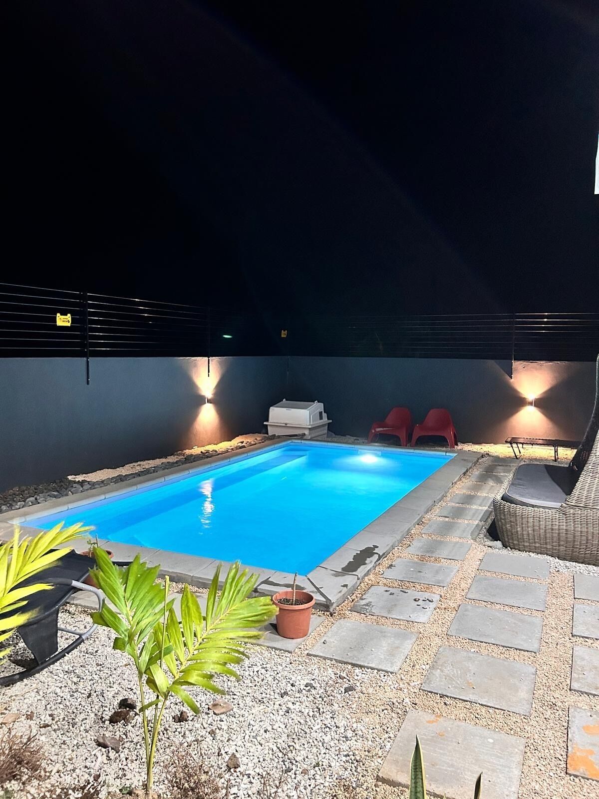 A swimming pool with a tiled deck, surrounded by potted plants and red chairs.