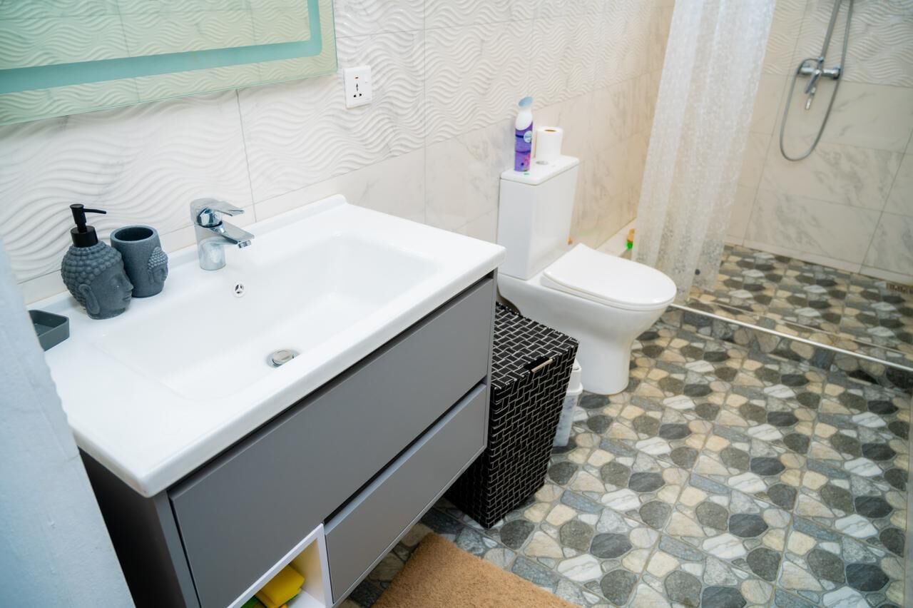 Une salle de bain avec un lavabo blanc, un meuble gris et des toilettes.