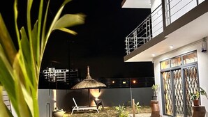 A modern building with a covered outdoor seating area, a thatched-roof structure, and potted plants. - Villa boulevard Paradise ideal for relaxing at will with family or friends (Grand Baie)