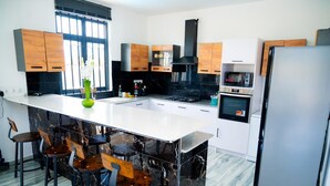 A modern kitchen with a marble island, bar stools, a stove, oven, microwave, and a refrigerator. - Villa boulevard Paradise ideal for relaxing at will with family or friends (Grand Baie)