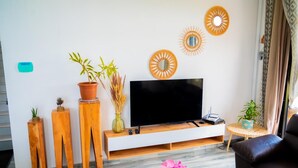 A modern living room with a flat-screen TV, wooden side tables, potted plants, and decorative wall art. - Villa boulevard Paradise ideal for relaxing at will with family or friends (Grand Baie)