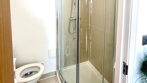 Une petite salle de bain située dans un coin, avec une douche à parois de verre, des toilettes et un lavabo blanc.