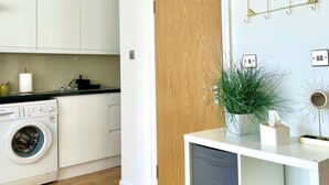 Une cuisine moderne avec des meubles blancs, un lave-linge Bosch, un plancher en bois et une porte en bois.