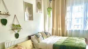Une chambre avec un lit, un canapé, une plante suspendue et des œuvres d’art aux murs.