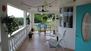 A covered outdoor area with a table and chairs, a door, and a view of greenery. - Sunny Villa Mar Chiquita, WE HAVE WATER  & Game room-beach hopping paradise (Tierras Nuevas Poniente)