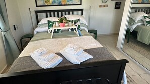 A neatly made bed with pillows and a tray of toiletries, a painting of a cityscape on the wall, and clocks indicating different time zones. - Sunny Villa Mar Chiquita, WE HAVE WATER  & Game room-beach hopping paradise (Tierras Nuevas Poniente)