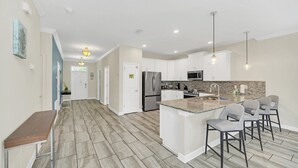 A modern kitchen with white cabinets, a granite countertop, and a stainless steel refrigerator. There are three bar stools and pendant lights above the counter. - EV_9036 - 9 Bed 5 Bath Villa with Screened-In Private Pool with Spillover Spa (Davenport)