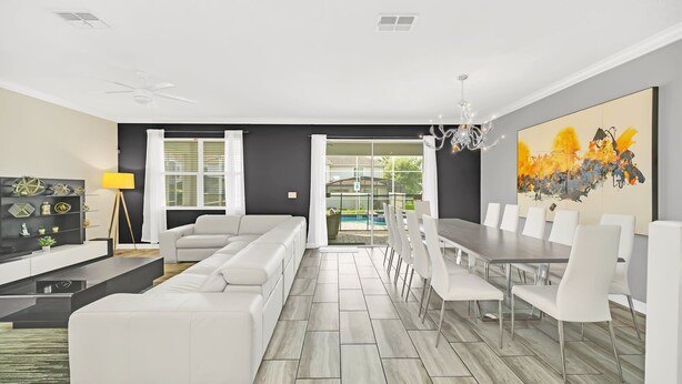 A modern living room with a sectional sofa, a dining area with a long table and chairs, and a large abstract painting on the wall. - EV_9036 - 9 Bed 5 Bath Villa with Screened-In Private Pool with Spillover Spa (Davenport)