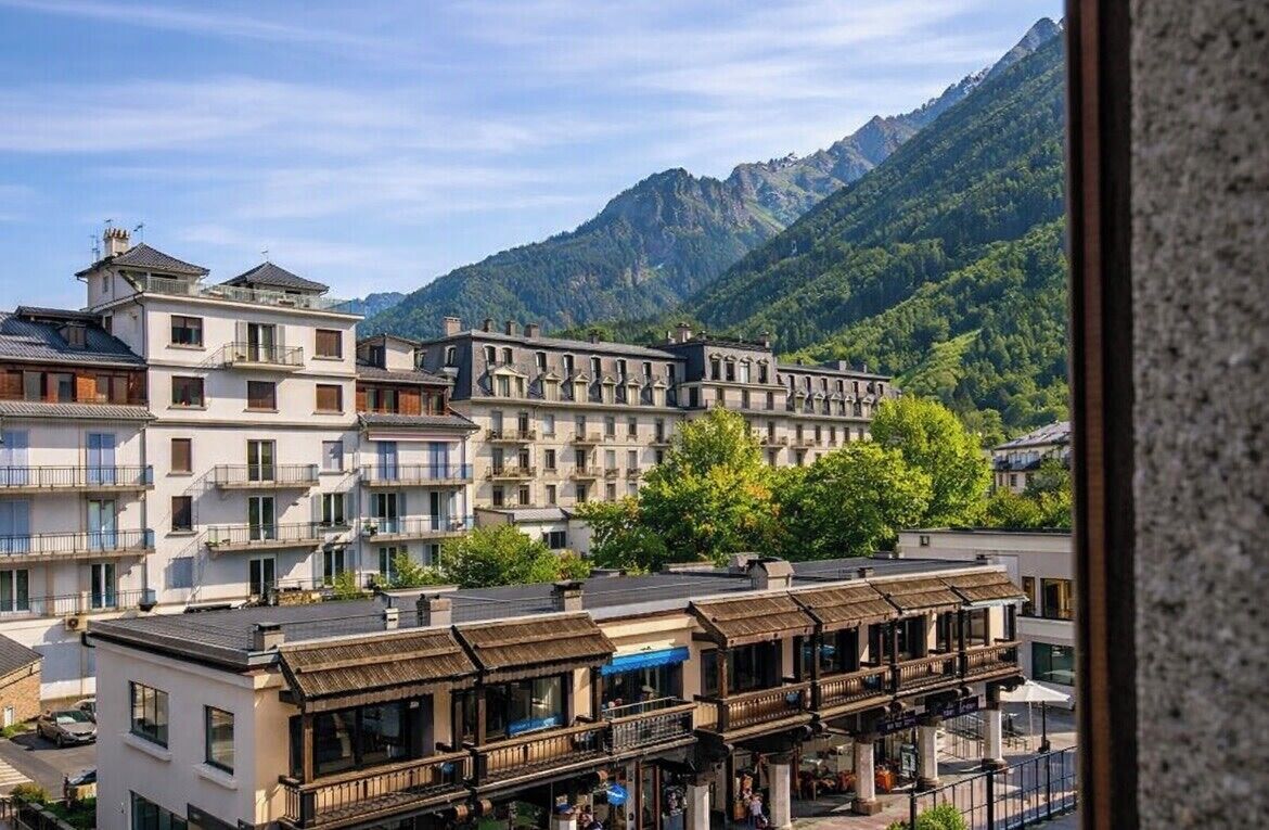 A town with multi-story buildings, a restaurant with outdoor seating, and mountains in the background.