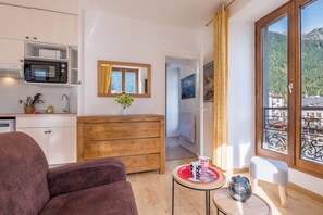 A compact kitchen with a microwave, a wooden dresser, and a dining area with a table and chairs. - Charming flat right in the city centre (Chamonix-Mont-Blanc)