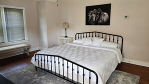 Ein Schlafzimmer mit Bett, Nachttisch, Lampe, Sitzbank, Deckenventilator und Wandthermostat.