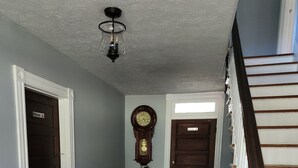 Ein Flur mit Holzboden, einer Großvateruhr, einem Blumentopf und einer Treppe mit weißen Geländern.