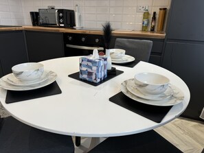 Una mesa redonda para comer con cuatro cuencos y platillos blancos, una caja de pañuelos y un adorno sobre un mantel individual negro.