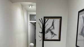 Un couloir doté d’un parquet en bois disposé en chevrons, d’une rambarde blanche et d’un lampadaire noir, le tout agrémenté d’une peinture abstraite contemporaine.