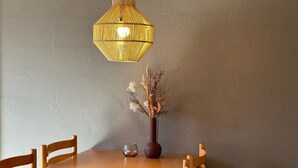 Une table à manger en bois, des chaises, un luminaire suspendu et un vase contenant des fleurs séchées.
