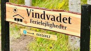 Un panneau en bois indiquant « Vindvadedet Ferielejighedsheder » et la direction du parking.