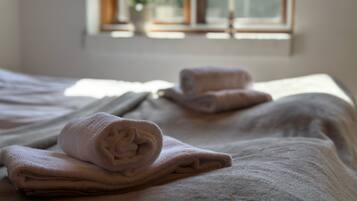 A neatly made bed with rolled towels and a window with a view of greenery outside.