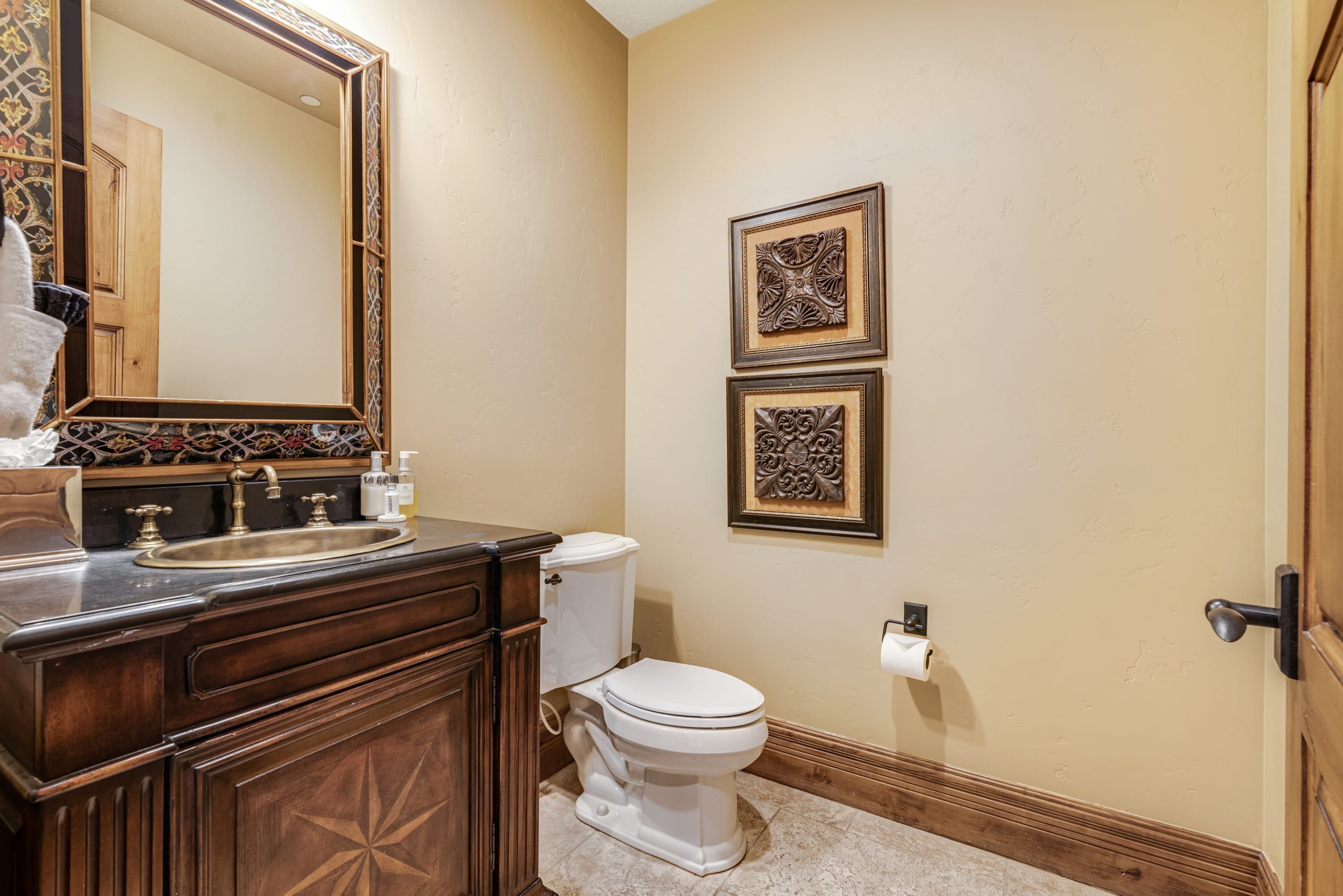 Un baño con tocador de madera, lavamanos, inodoro y dos elementos decorativos en la pared.