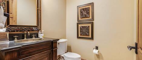 Un baño con tocador de madera, lavamanos, inodoro y dos elementos decorativos en la pared.