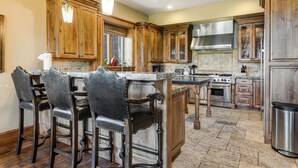 A spacious kitchen with wooden cabinets, a large island with bar stools, a stainless steel range hood, and a built-in oven. - Gorgeous Deer Valley Home Minutes From the Slopes (Park City)
