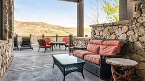 An outdoor patio with wicker furniture, a stone wall, and a view of a hilly landscape. - Gorgeous Deer Valley Home Minutes From the Slopes (Park City)
