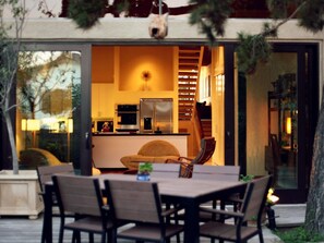 Un espace de vie ouvert comprenant un coin repas avec table et chaises, une cuisine équipée d’appareils modernes et une grande fenêtre donnant sur un jardin.