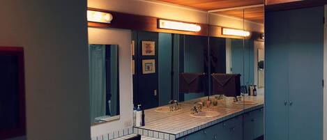 A modern bathroom with a large mirror, two sinks, and a chair.