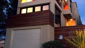 Une maison moderne à deux étages, dotée d’un garage, de grandes fenêtres et d’un jardin bien entretenu agrémenté de rochers et de plantes.