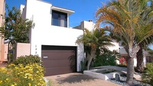 A modern two-story house with a brown garage, surrounded by palm trees and a variety of plants. - Stunning View Mission Bay Luxury Home Private Pool (San Diego)