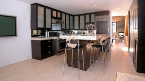 A modern kitchen with dark cabinetry, a central island with bar stools, and a dining area. - Stunning View Mission Bay Luxury Home Private Pool (San Diego)