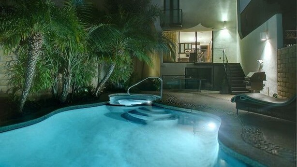 A swimming pool with steps leading into it, surrounded by palm trees and a building with a balcony. - Stunning View Mission Bay Luxury Home Private Pool (San Diego)