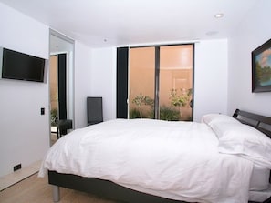 A modern bedroom with a large bed, a TV mounted on the wall, and a sliding glass door leading to a balcony with plants. - Stunning View Mission Bay Luxury Home Private Pool (San Diego)