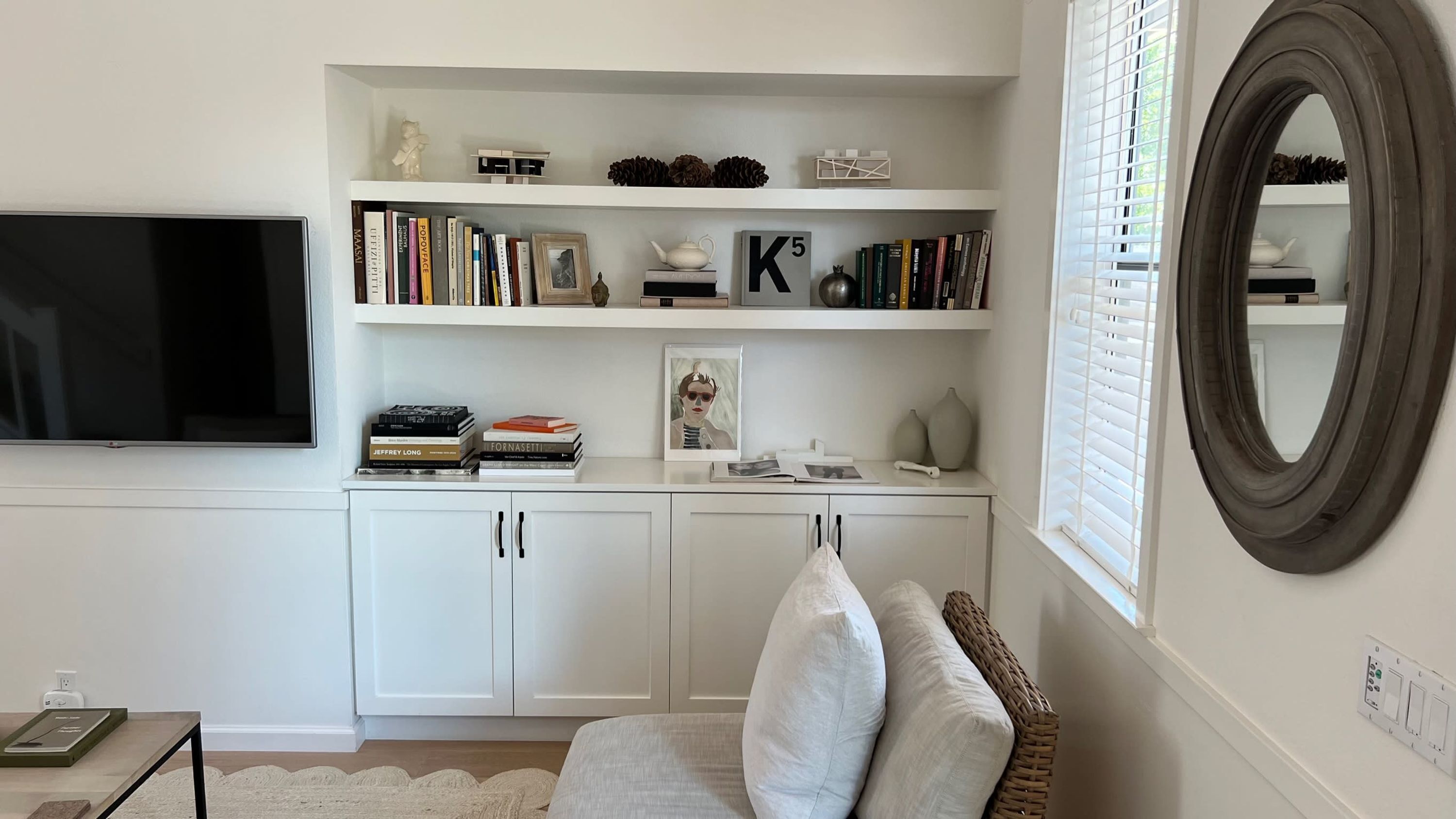 A living room with a white TV, bookshelves, a framed picture, and a mirror.