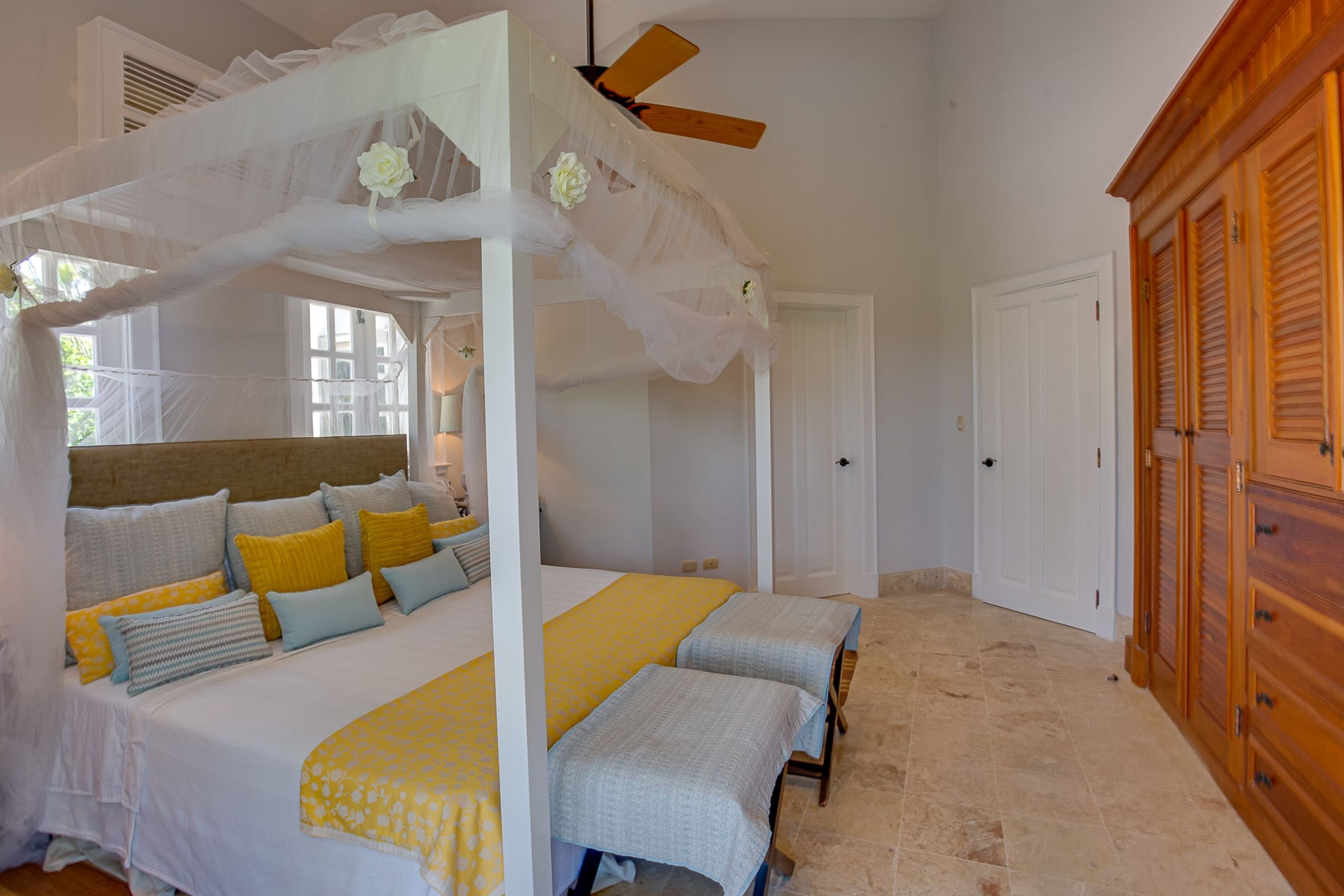 A bedroom with a canopy bed, two bedside tables, a wooden wardrobe, and a door.