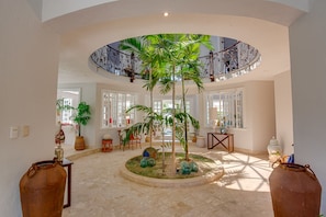 Relax in a serene space with a central circular area featuring lush plants and decorative items, surrounded by comfortable seating and natural light.