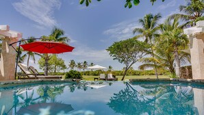A clear swimming pool with lounge chairs and umbrellas, surrounded by palm trees and a clear sky. - Villa Tortuga in Punta Cana (Punta Cana)