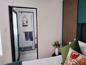 Une chambre d’hôtel avec un lit, une table de chevet ornée d’un vase, un oreiller vert et une porte donnant sur une salle de bain.