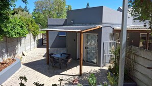 A covered patio area with a table and chairs, surrounded by a brick patio and a garden. - Dee-ones at Witboom With Pool (Cape Town)