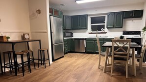 Et moderne køkken med grønne skabe, rustfrie hvidevarer, et træspisebord med stole og et barområde med barstole.