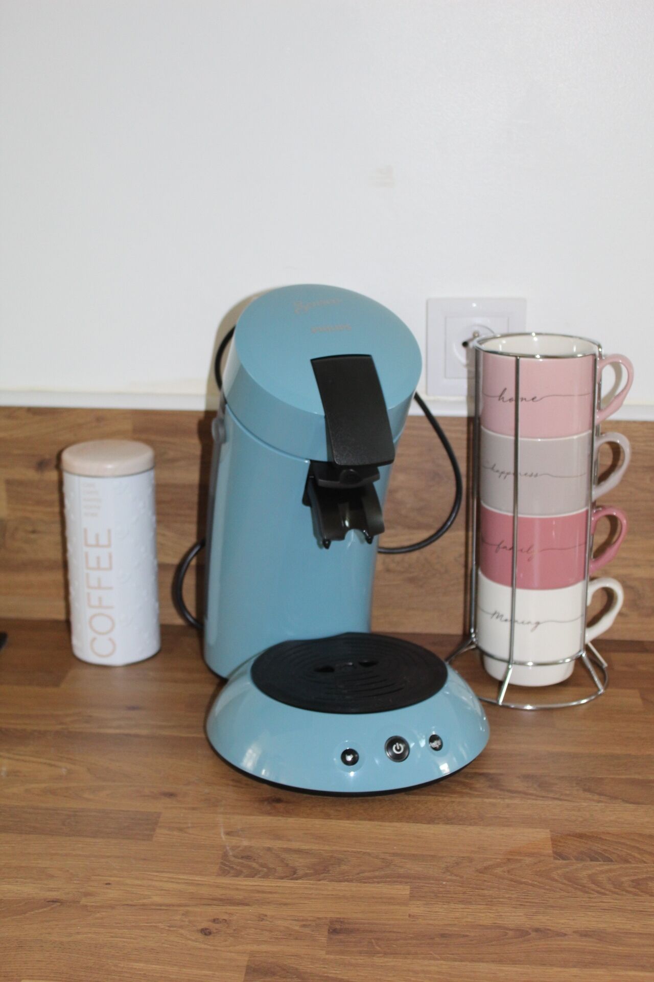 Une machine à café, un porte-tasse et un récipient à café, le tout posé sur un plancher en bois.